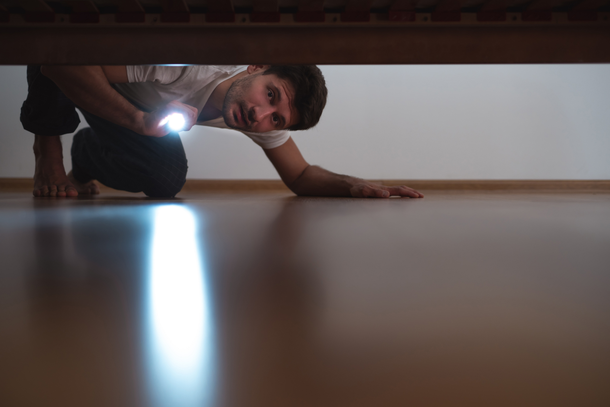 Man with a flashlight looking under the bed