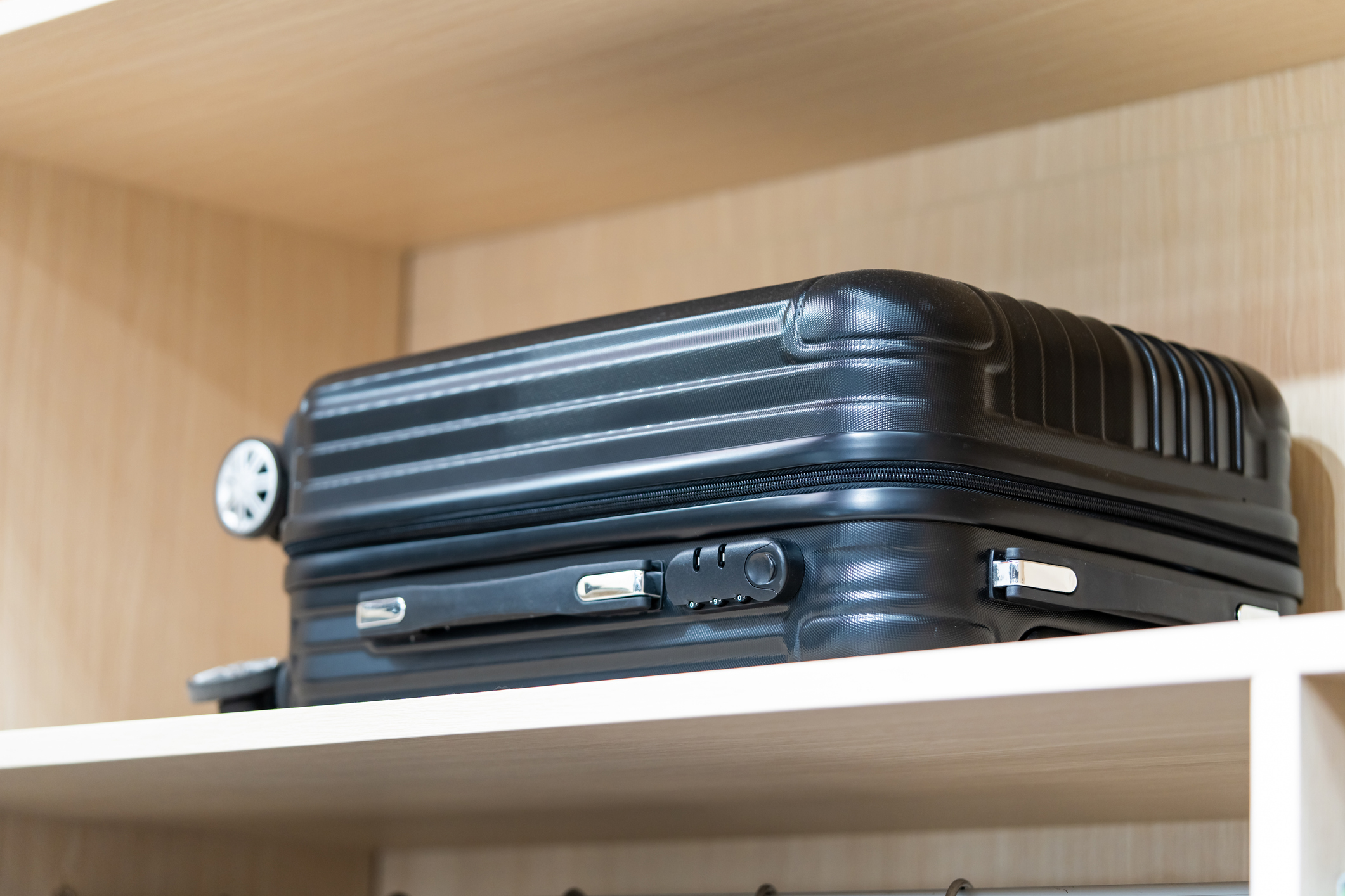 A black suitcase placed at the top of a white brown wood shelf.