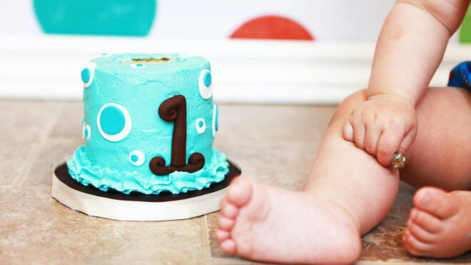 Blue first birthday cake next to baby.