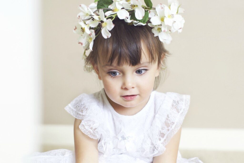 Toddler flower girl sits in a white dress looking off to the side