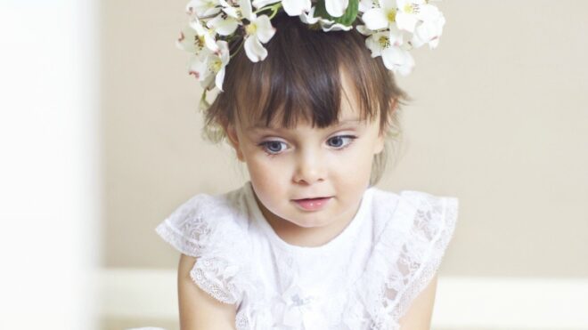 Toddler flower girl sits in a white dress looking off to the side