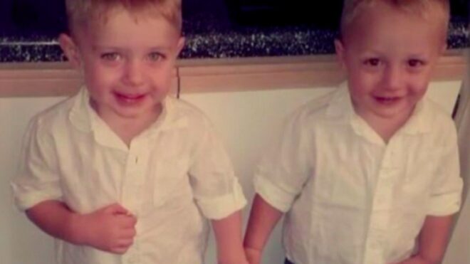 Noah and Levi Schroeder stand holding hands smiling.