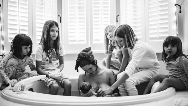 Casey Teller sits in a tub holding her newborn while surrounded by her five other daughters.