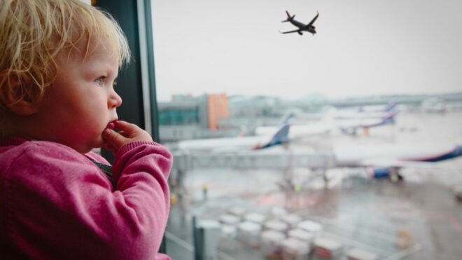 Young toddler looks out the window at a plane taking off.