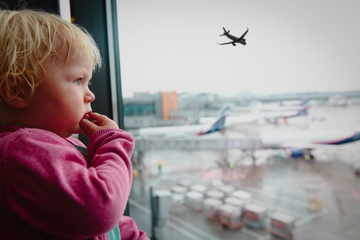 Young toddler looks out the window at a plane taking off.