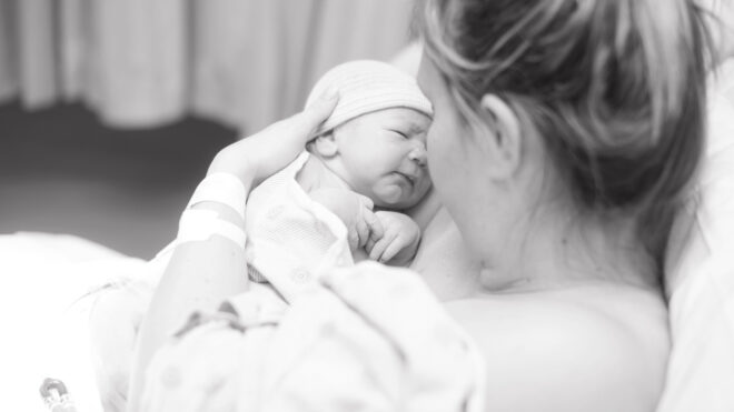 A black and white photo shows a mother cradling her infant shortly after giving birth.