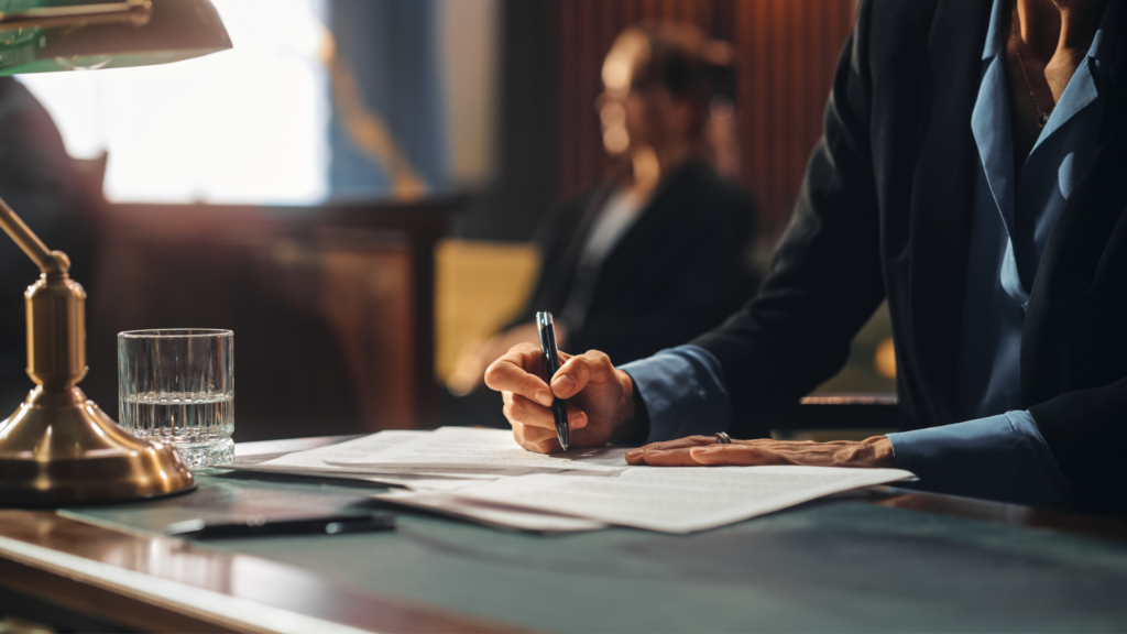 a woman in shadow sitting in courtroom seat, a closeup on a hand holding a pen