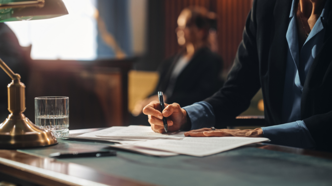 a woman in shadow sitting in courtroom seat, a closeup on a hand holding a pen