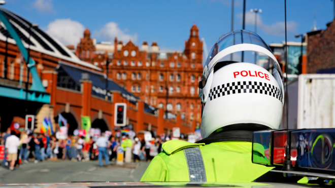 UK police in riot gear standing a distance away from people protesting