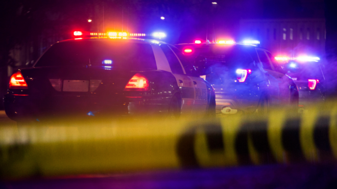 police cars lined up with their lights on and yellow police tape in the foreground