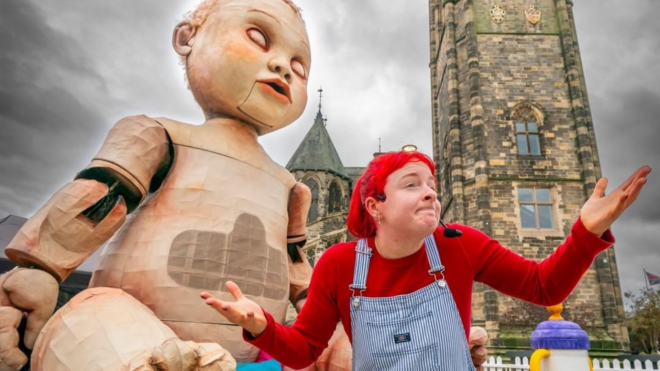 27-foot tall baby statue with a woman wearing a red wig in front of it