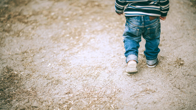 Toddler boy walks away on a dirt path.