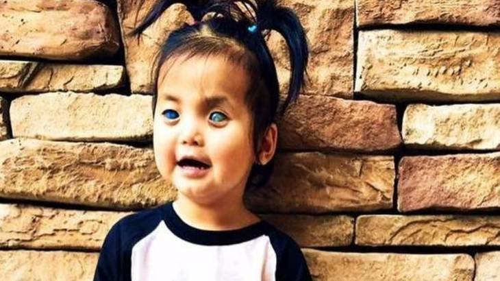 Primrose Austin smiles while wearing pigtails and standing in front of a stone wall.