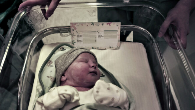 An infant baby lies in a bed while wheeled through the maternity ward.
