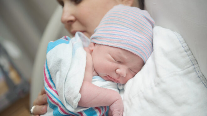 New mother cradles baby close while laying in a hospital bed.