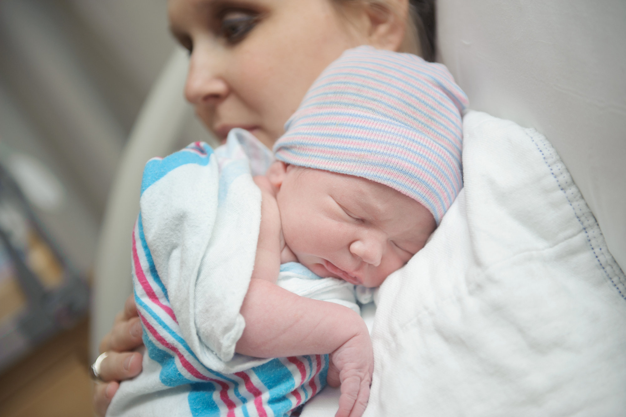 New mother cradles baby close while laying in a hospital bed.