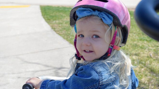 Girl looks back at camera while wearing pink bike helmet.