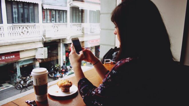 Woman sits in Starbucks with a coffee and muffin while texting.