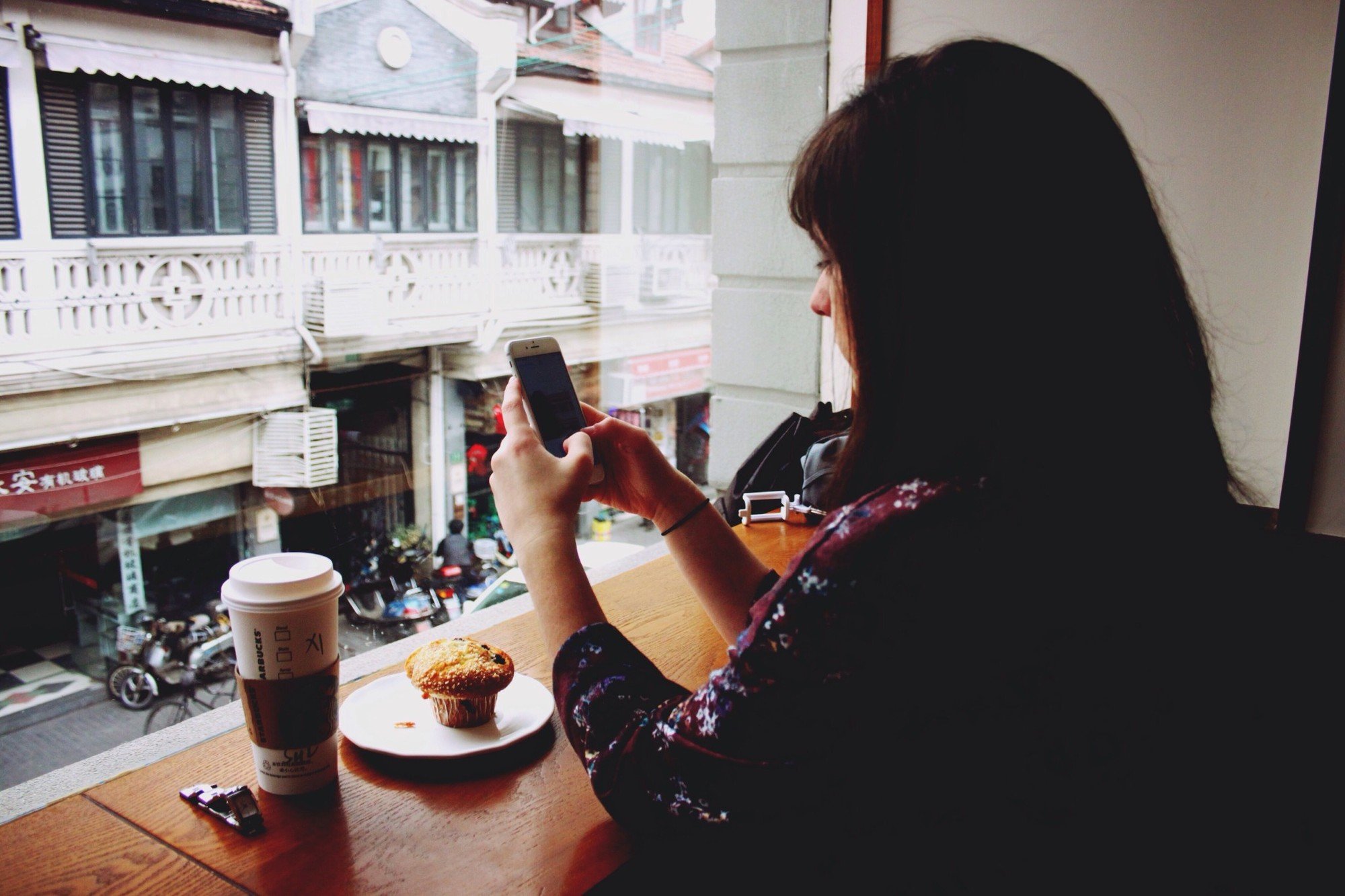 Woman sits in Starbucks with a coffee and muffin while texting.