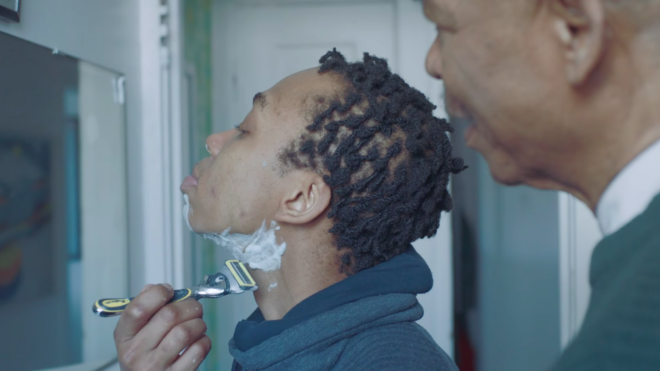 A young trans man attempts his first shave as his dad looks on.