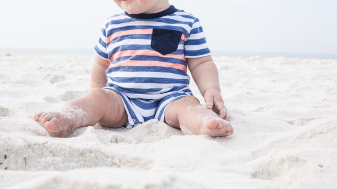 Toddler boy sits in sand on beach
