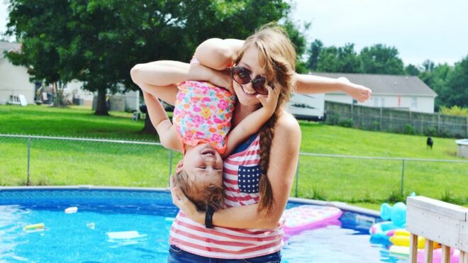 Mom hugs toddler close while standing in front of a pool