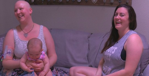 Lauren Miller smiles while sitting with a friend and holding her baby.