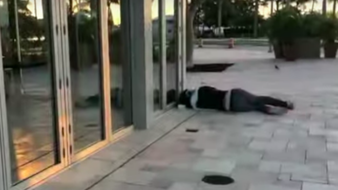 A homeless person sleeps near a building in the pavilion