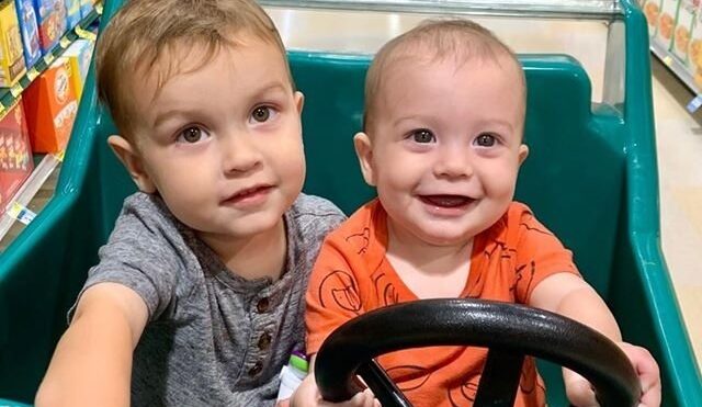 Two toddler boys smile while sitting in a shopping cart