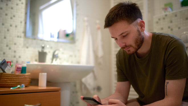 Man sits on toilet with phone