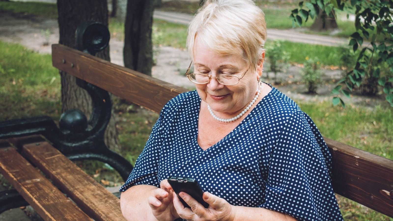 An older white woman with short white hair and glasses smiling down at her phone