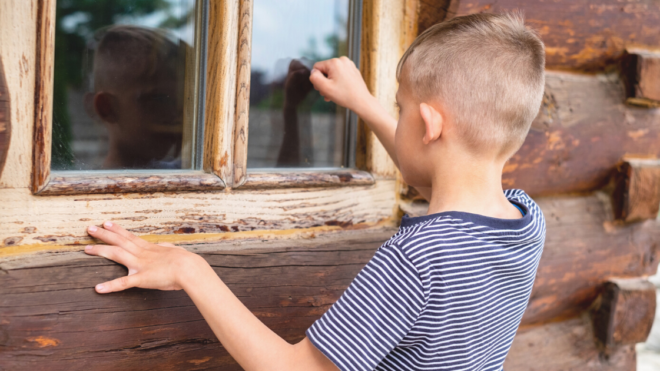 boy knocking on the window of a wood house