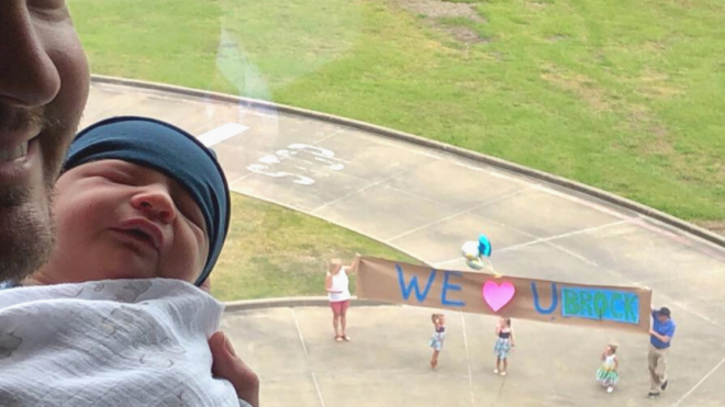 dad holding newborn siblings holding sign outside window
