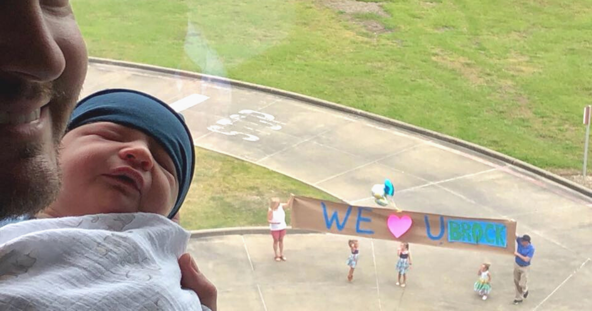 dad holding newborn siblings holding sign outside window