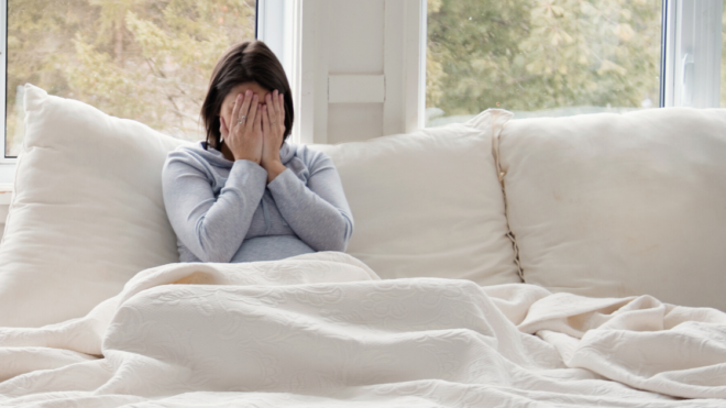 woman in bed with hands over face.