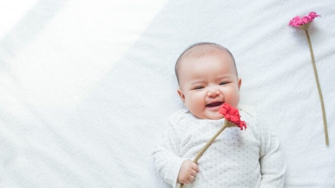 baby wearing white holding pink flowers