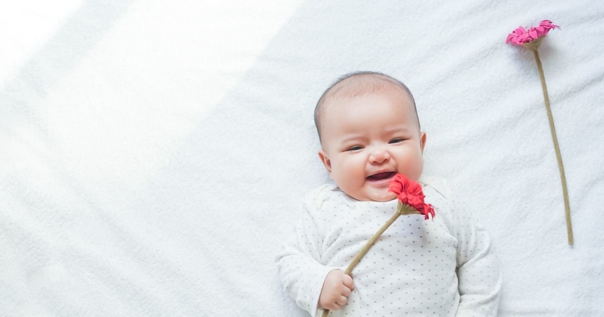 baby wearing white holding pink flowers