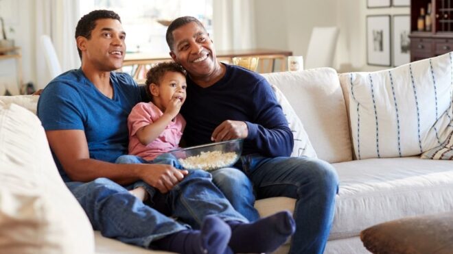 two dads and their child watching TV together
