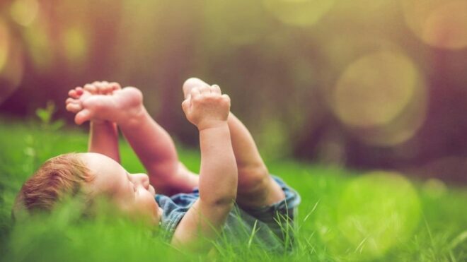 baby laying in the grass playing with feet