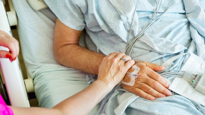 Wife holding sick husband's hand in hospital bed