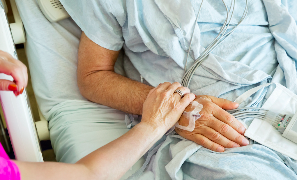 Wife holding sick husband's hand in hospital bed