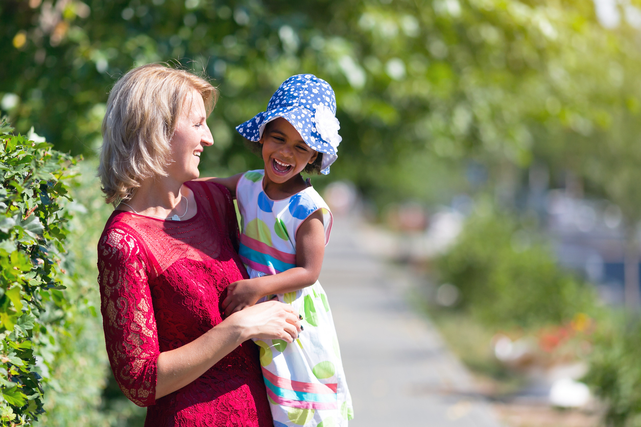 A white woman carries a black girl on her shoulder.