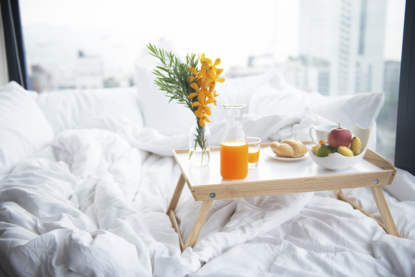 Soft breakfast food, orange juice, bread and milk on the small tabel on the white bed.