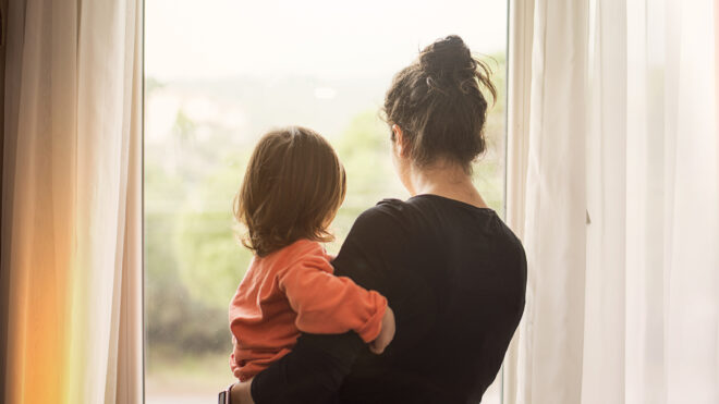 mother looking out window holding child