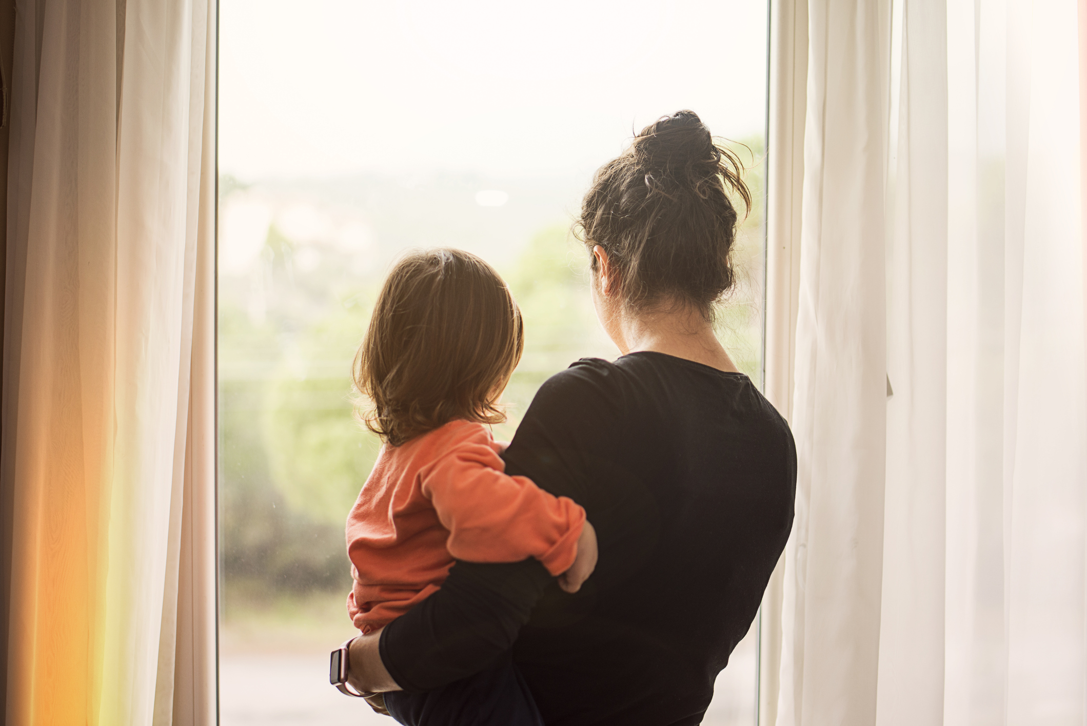 mother looking out window holding child