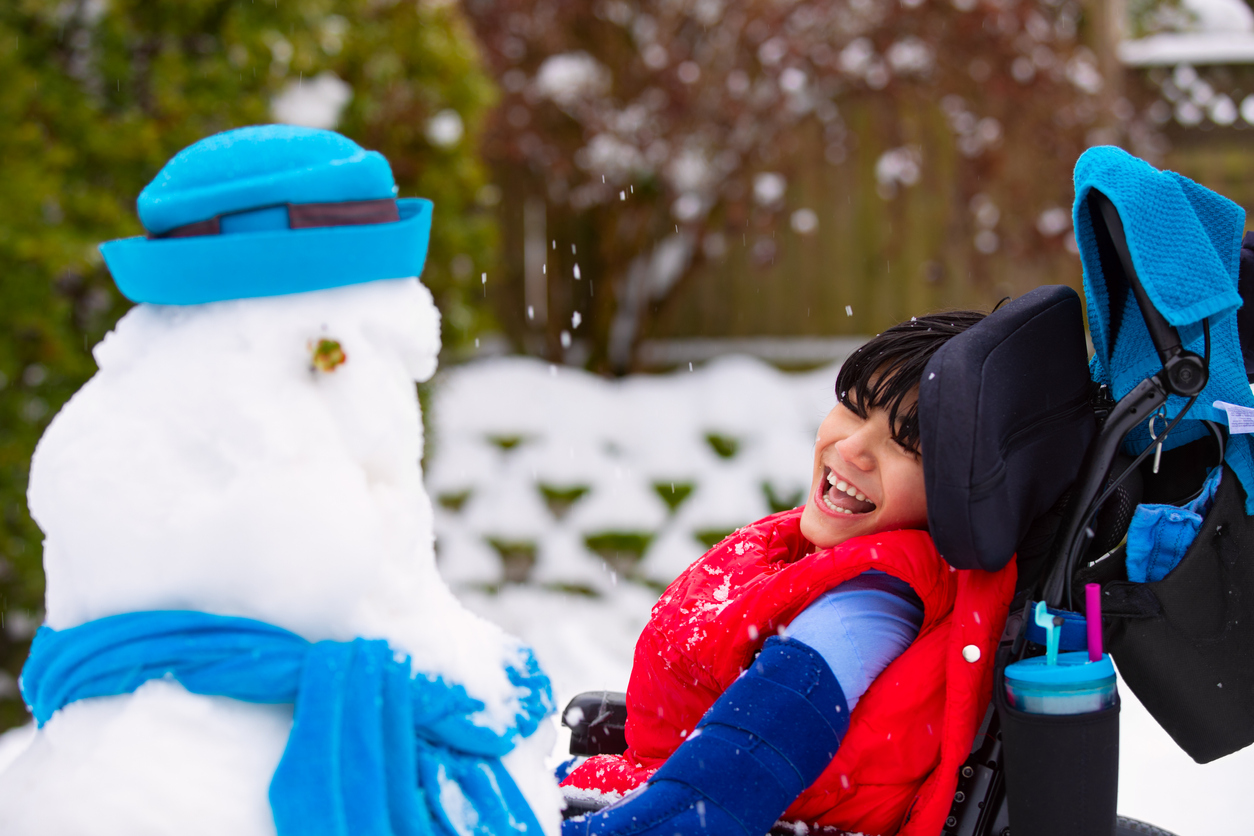 Happy smiling disabled boy in wheelchair building a snowman