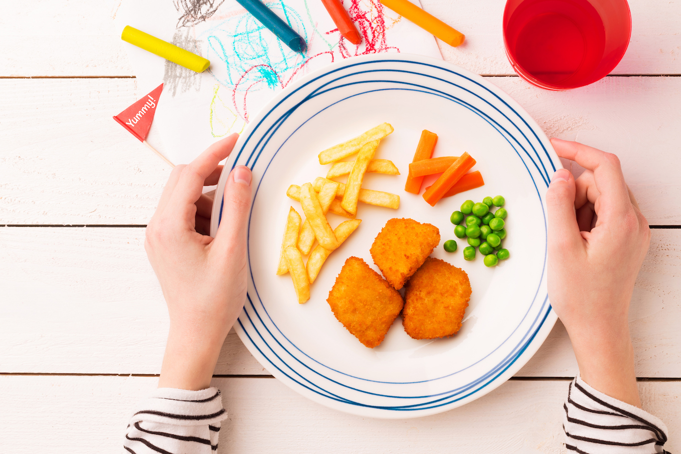 Meal (dinner) in child's hands - chicken nuggets, fries, green peas