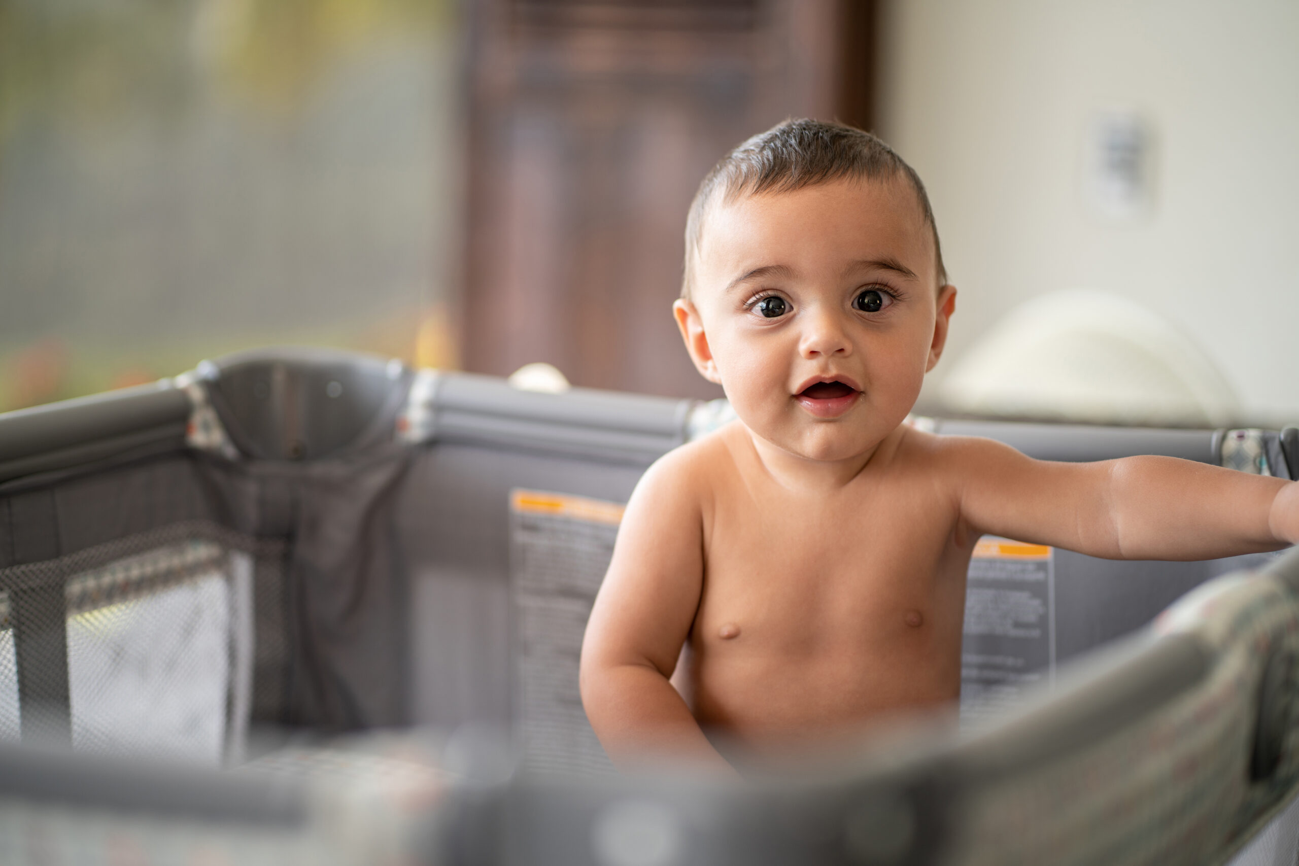 Cute little baby in playpen looking at camera with amazement