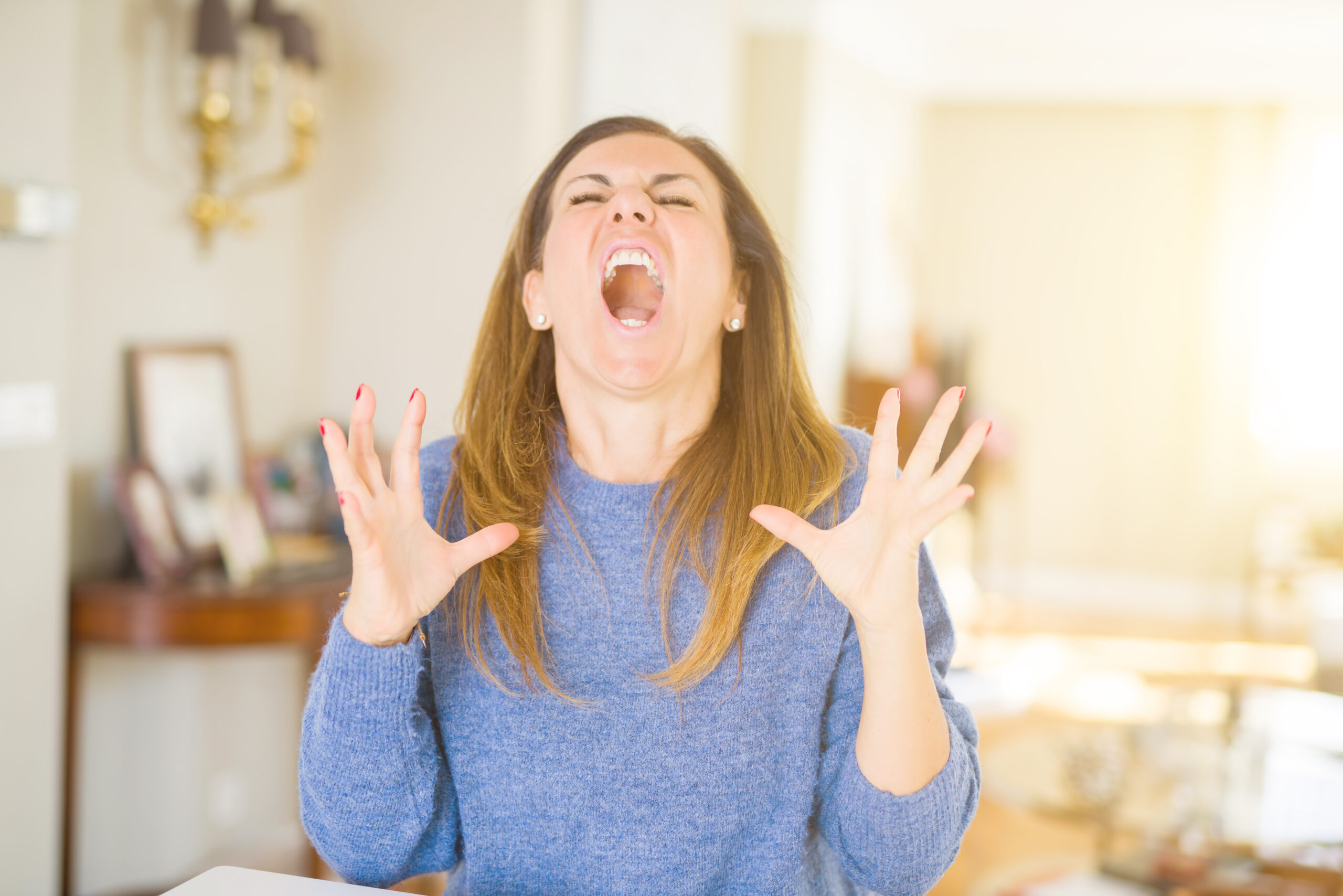 Beautiful middle age woman at home crazy and mad shouting and yelling with aggressive expression and arms raised. Frustration concept.