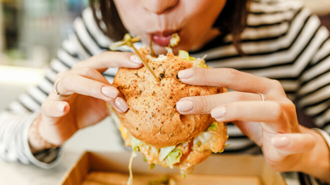 Asian woman eating a burger. He mouth is full and it looks like she just took a big bite.